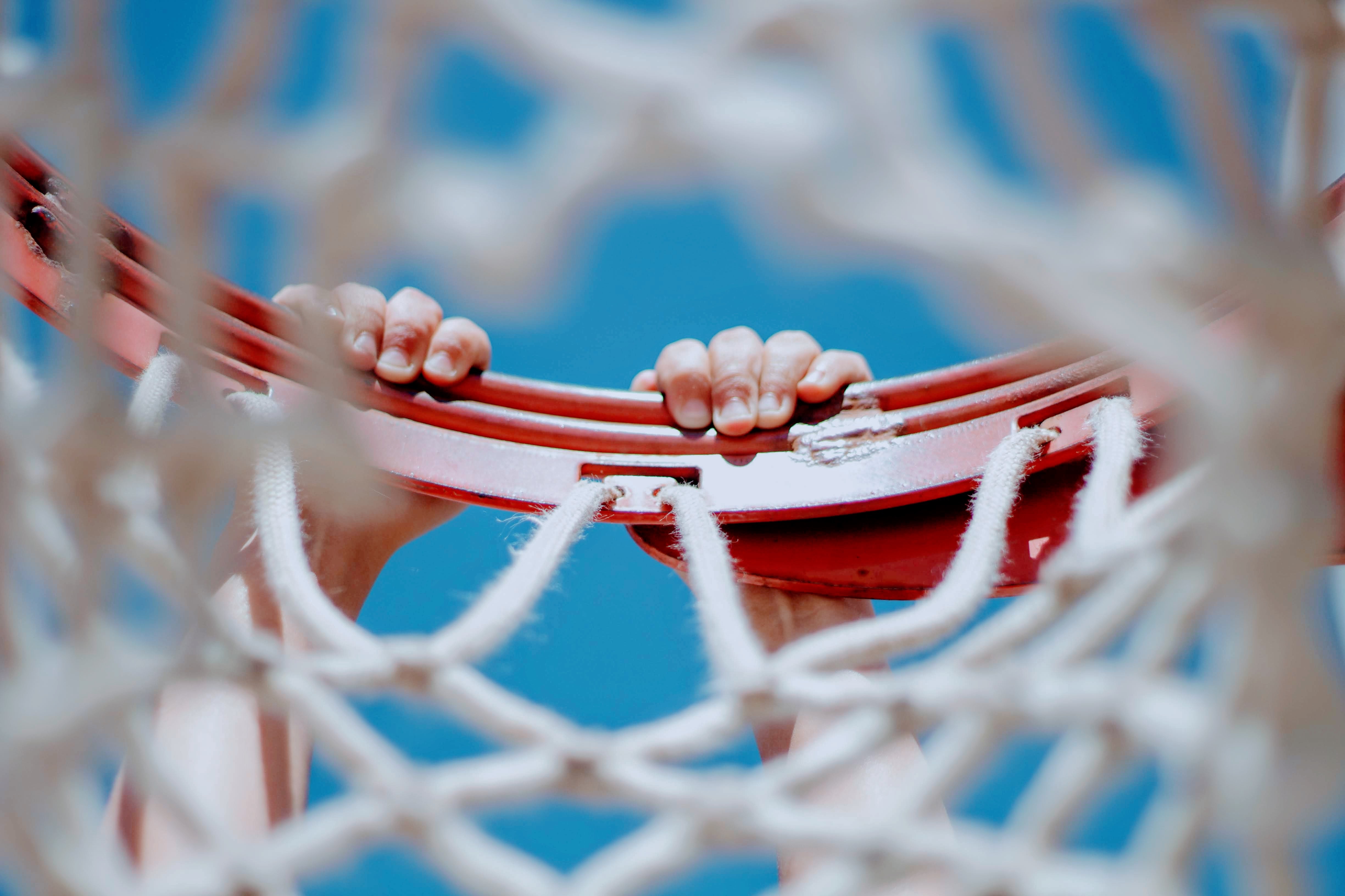 hands hanging from a basketball net